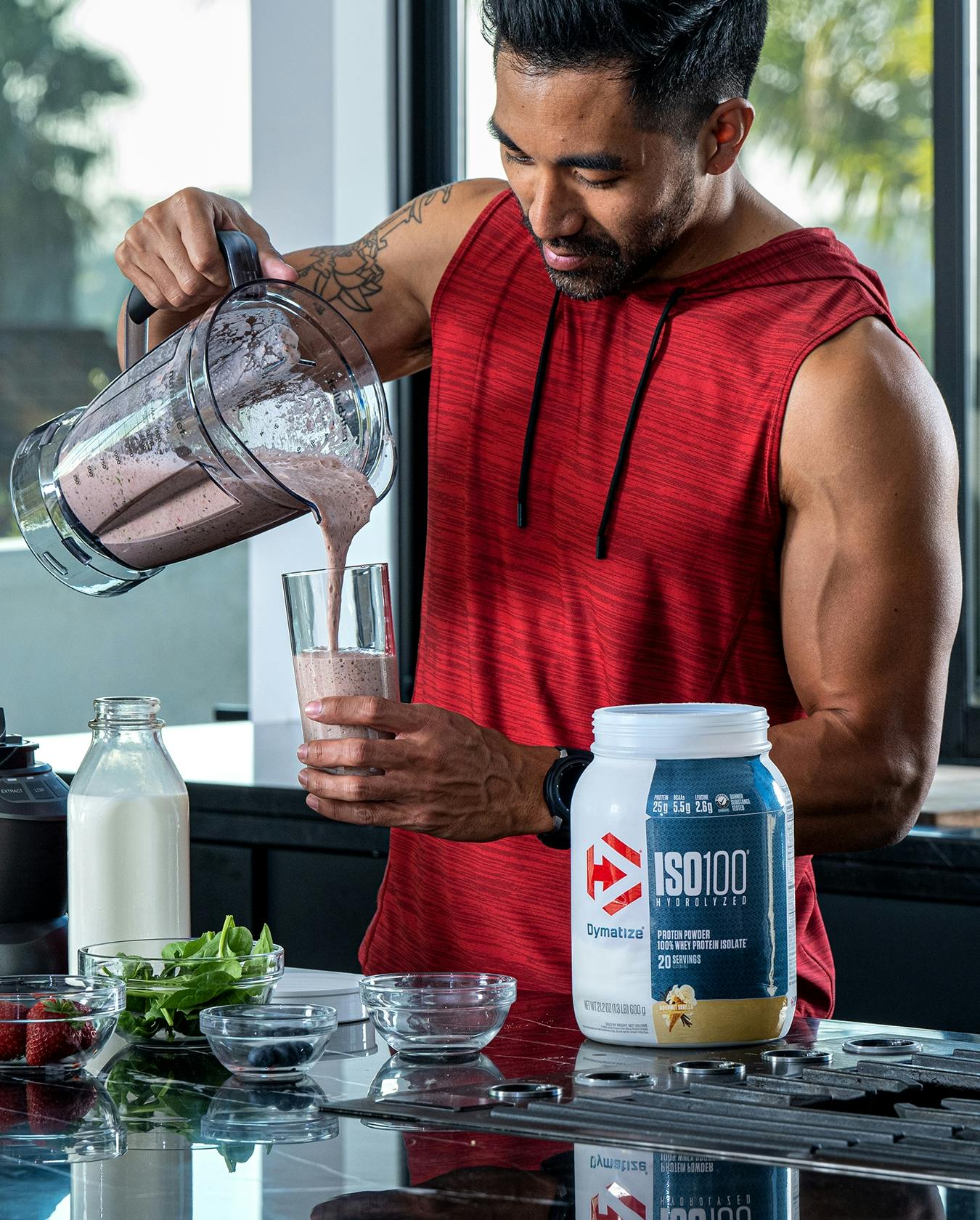 A man in his kitchen, pouring a Dymatize protein shake out of his blender.