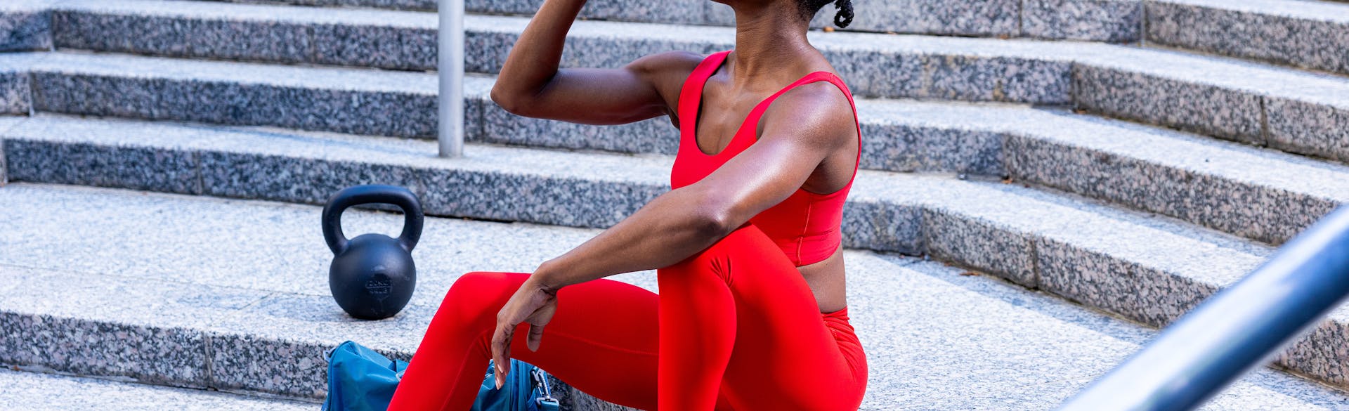 A woman in workout gear sitting on steps and drinking a Performance Protein Shake